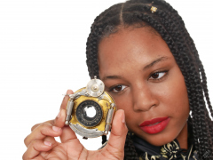 Caleann in tight black-and-gold Cheongsam examines Bausch & Lomb shutter c/w Beck lens assembly