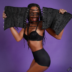 Caleann in black sixties-style bra and girdle, looking thorugh the lases of a black underbust corset