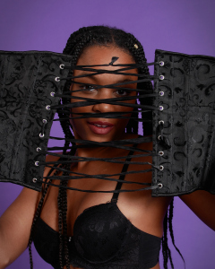 Caleann in black sixties-style bra and girdle, looking thorugh the lases of a black underbust corset