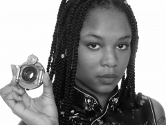 Caleann in tight black-and-gold Cheongsam examines Bausch & Lomb shutter c/w Beck lens assembly