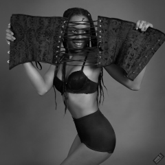 Caleann in black sixties-style bra and girdle, looking thorugh the lases of a black underbust corset