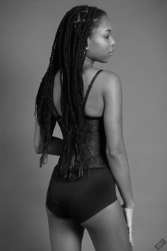 Rear view of Caleann in tightly-laced black underbust corset, worn over black sixties-style bra and girdle
